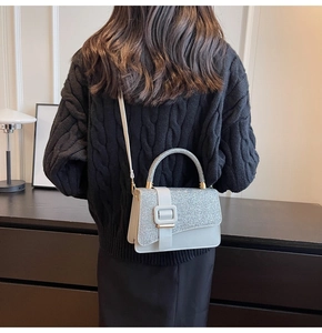 Model wearing white sequin crossbody bag with gold hardware against a black knit sweater
