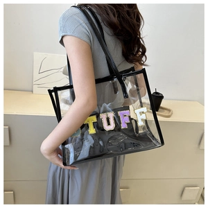 Close-up of clear PVC tote with black leather trim and colorful glitter STUFF lettering