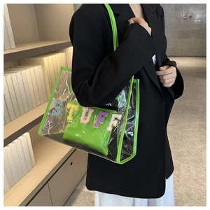 Detail of transparent PVC tote bag with green leather handles and plush STUFF patch