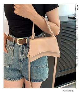 Fashionable beige hourglass handbag with knotted handle and curved base worn by a model