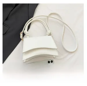 Detail view of white leather handbag with twisted handle and smartphone for size reference