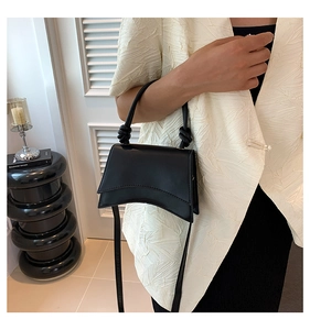 Close-up of minimalist black leather crossbody bag featuring a curved base and knot handle