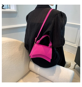 Side view of a hot pink hourglass bag with a unique curved base on a textured background