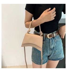Detail view of beige mini crossbody bag with a curved base and knotted rope handle design