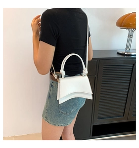 White minimalist crossbody bag with unique curved base and knotted handle on a model