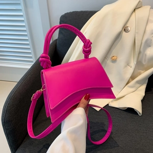 Detail of a bright magenta hourglass bag with knotted handle on a soft grey chair