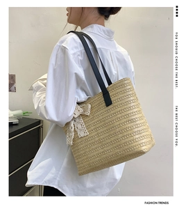 Detail of straw tote bag featuring black leather straps and a delicate white lace bow