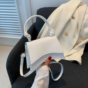 White leather handbag with curved base and knot handle shown in a lifestyle setting