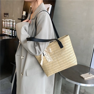 Large beige woven straw tote bag with black straps and a white lace bow detail