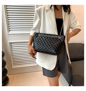 Sac fourre-tout noir matelassé avec chaîne dorée porté par un mannequin en bureau