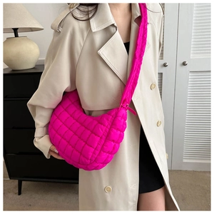 Side view of a bright pink quilted crossbody puffer bag worn with a beige trench coat
