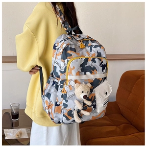 Detailed view of camo backpack with multi-layered zippers and a cute plush bear charm