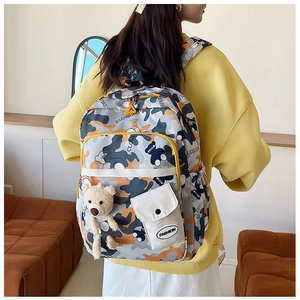 Detail of camouflage backpack with yellow trim, fashion patch, and plush bear charm