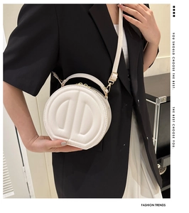 Close-up of a white quilted round handbag styled with a black blazer and white skirt