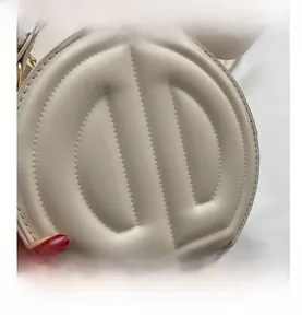 Close-up of beige quilted circular bag with 3D letter design and gold hardware