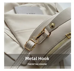 Close-up of golden metal hooks and quilted texture on a minimalist cream crossbody bag