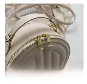 Detailed close-up of smooth dual golden zippers on a minimalist cream round handbag