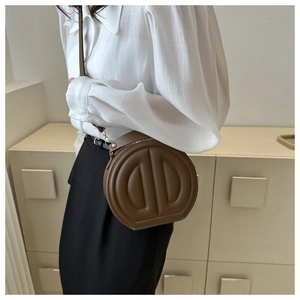 Detail of dark brown circular handbag with embossed geometric design and gold buckle