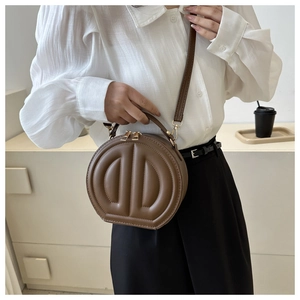 Detail of a brown round crossbody bag featuring geometric 3D embossing and gold hardware