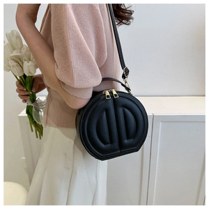 Detail view of the black round shoulder bag featuring chic embossed patterns and golden zippers