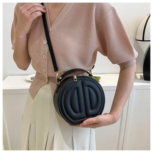 Detail of black round crossbody bag with embossed letters and gold zipper on a model