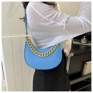 Close-up of sky blue half-moon bag featuring textured faux leather and chunky gold chain