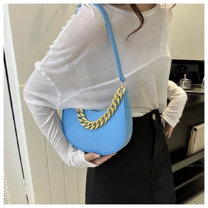 Detail of bright blue crescent underarm bag with bold gold chain and soft felt texture