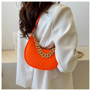 Detail of bright orange faux-croco shoulder bag with a bold gold chain on a white blazer
