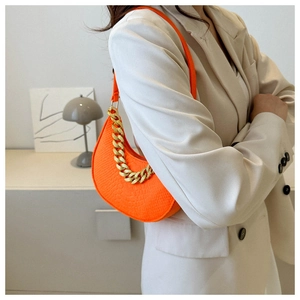 Detail of bright orange faux leather bag with crocodile texture and gold chain link strap
