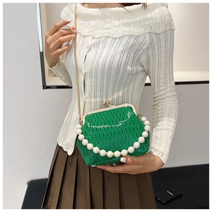 Detail of green woven kiss-lock bag with white pearl handle and gold chain strap