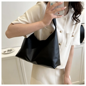 Close-up of a minimalist black crescent hobo bag held by a model in a beige tweed outfit