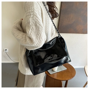 Detailed view of black patent leather tote bag featuring elegant metal chain strap on model