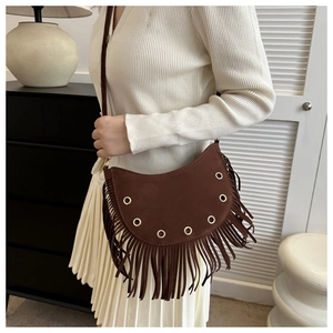 Detail shot of brown suede tassel crossbody bag with crescent shape and metal grommets