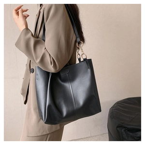 Classic black leather tote bag with wide strap and gold hardware on model in beige
