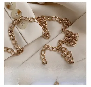 Détail d'une bandoulière en chaîne dorée brillante posée sur un blazer beige pour sac femme
