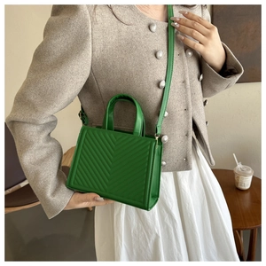 Detail of green quilted crossbody bag with V-shaped stitching and golden hardware detail