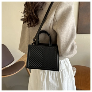 Detail of black quilted PU leather crossbody bag with V-pattern and gold hardware