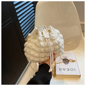 Détail du sac seau blanc en tissu texturé avec cordon de serrage et bandoulière dorée