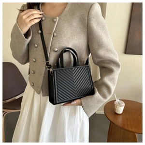 Detail of black quilted crossbody bag with gold buckle on a minimalist table
