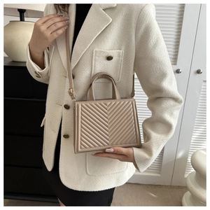 Quilted beige handbag with V-shaped stitching held by a model in a tweed jacket