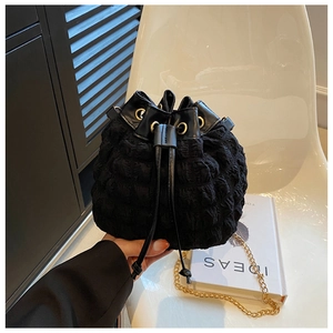 Détail d'un sac seau noir en tissu gaufré avec cordon de serrage et chaîne dorée