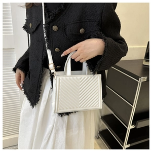 Detail of white V-quilted square handbag with slim shoulder strap and metal hardware