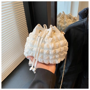 Détail du tissu blanc plissé à bulles et de la chaîne dorée sur le sac seau à cordon