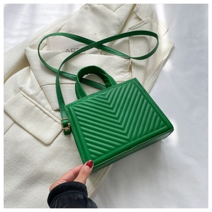 Close-up of green quilted square bag with V-shaped stitching on white blazer jacket