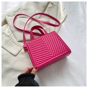 Detail of fuchsia chevron quilted bag with gold hardware and top handle on white blazer