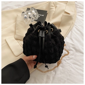 Détail d'un sac seau noir à texture bulle avec une élégante bandoulière en chaîne dorée