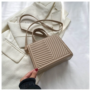 Detail of beige rectangular bag featuring V-shaped quilting and gold-tone hardware
