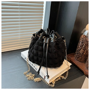 Détail d'un sac seau noir à bulles avec chaîne dorée posé sur des livres décoratifs