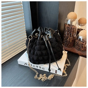 Détail du sac seau noir à texture bulle avec bandoulière chaîne sur un livre décoratif