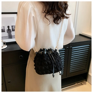 Détail d'un sac seau noir texturé avec chaîne dorée porté par un mannequin